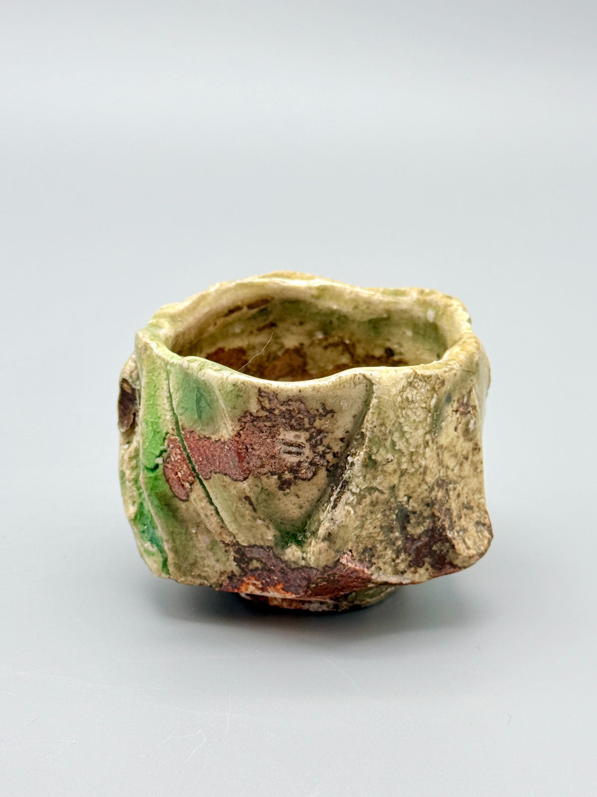Side view of Atarashi Manabu Iga cup showing green glaze beside mottled reddish-brown planes.