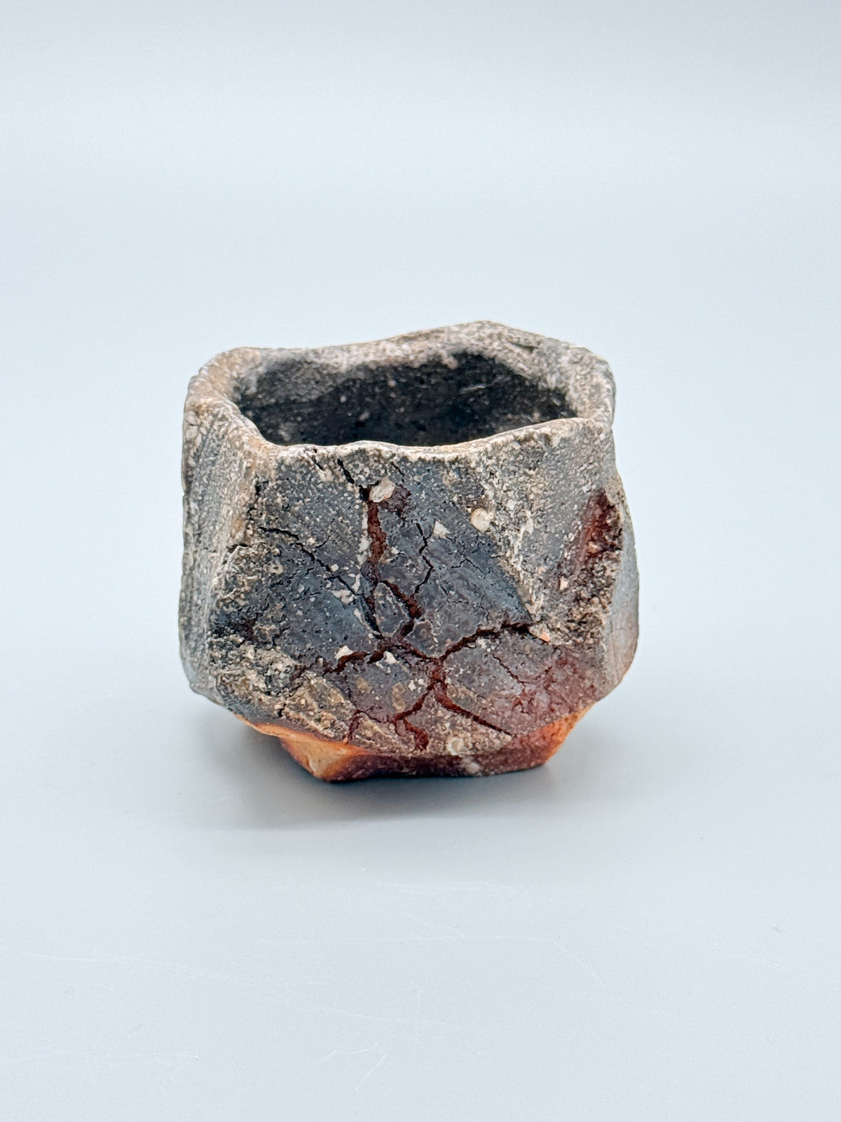 Atarashi Manabu hikidashi black Iga kurinuki cup with iron-grey planes, white mineral inclusions and warm clay at the foot.