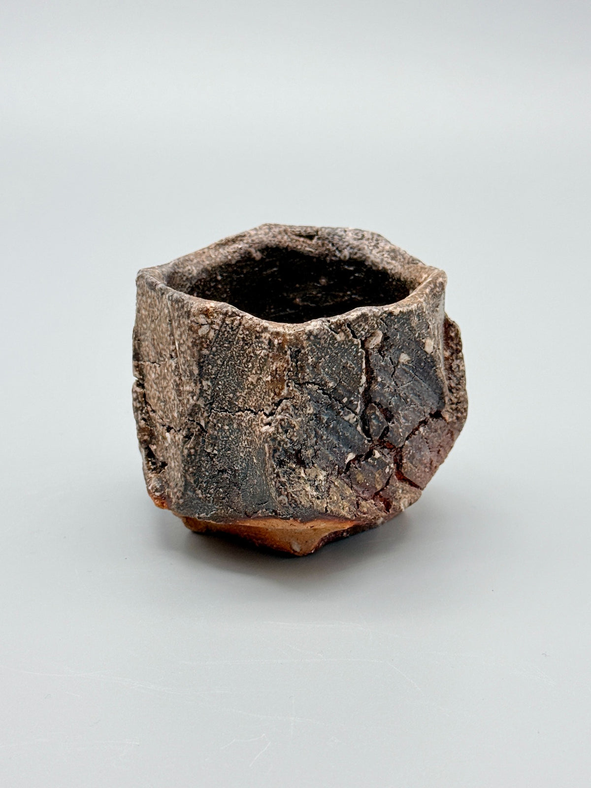 Angled view of Atarashi Manabu hikidashi black Iga cup with carved planes and an irregular rim.