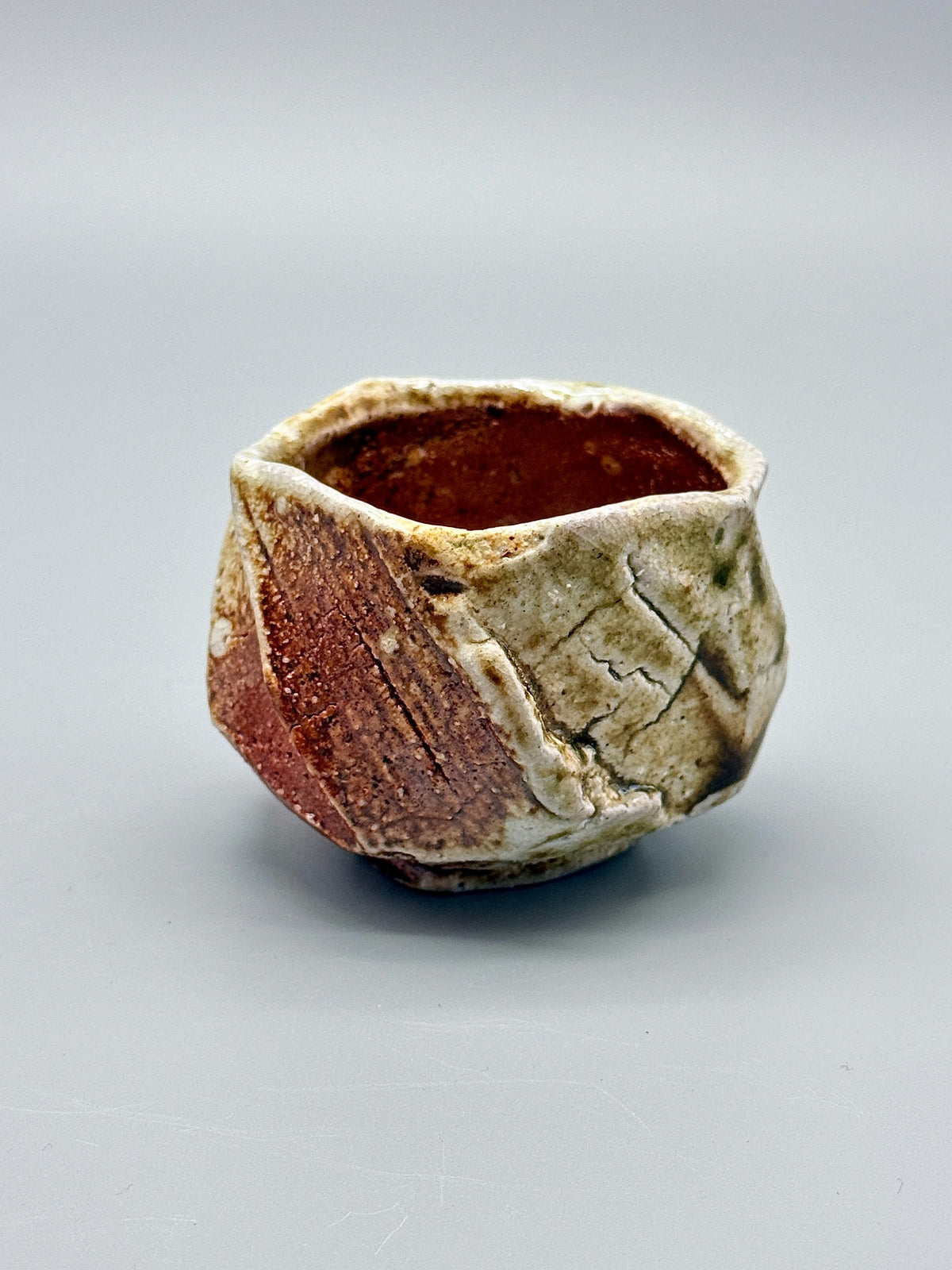 Reverse of Atarashi Manabu Iga cup showing broad reddish-brown planes beside pale glazed surfaces.