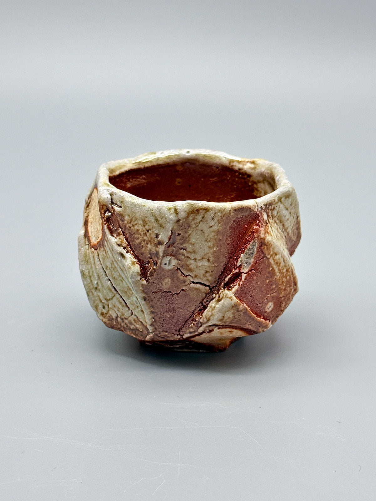 Angled view of Atarashi Manabu Iga cup with diagonal carved ridges and an uneven rim.