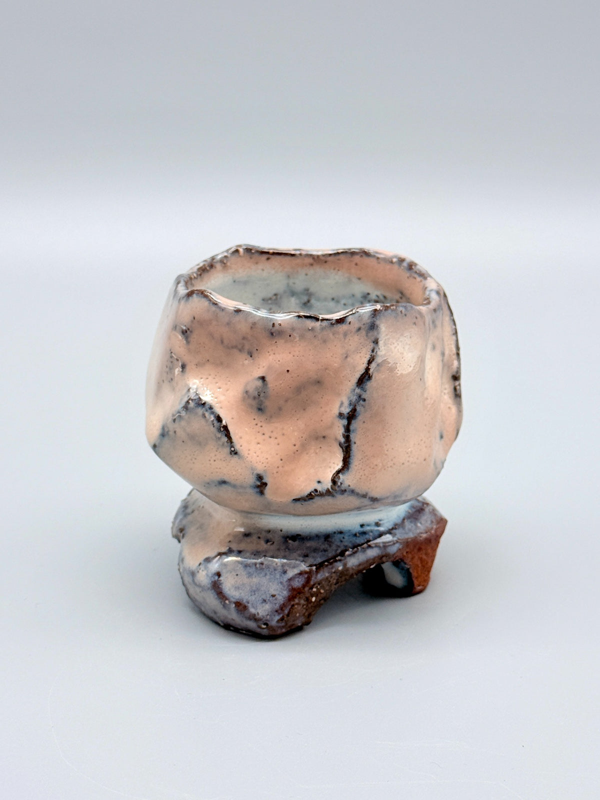 Angled view of Kaneta Masanao footed cup, showing uneven contours and exposed reddish-brown clay.